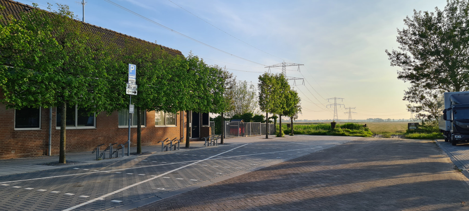 Parkeerstroken en fietsenrekken langs de gevel van het gebouw, met het polderlandschap op de achtergrond.