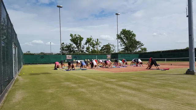 Een groep mensen doet yoga op matten op een tennisbaan in de buitenlucht.