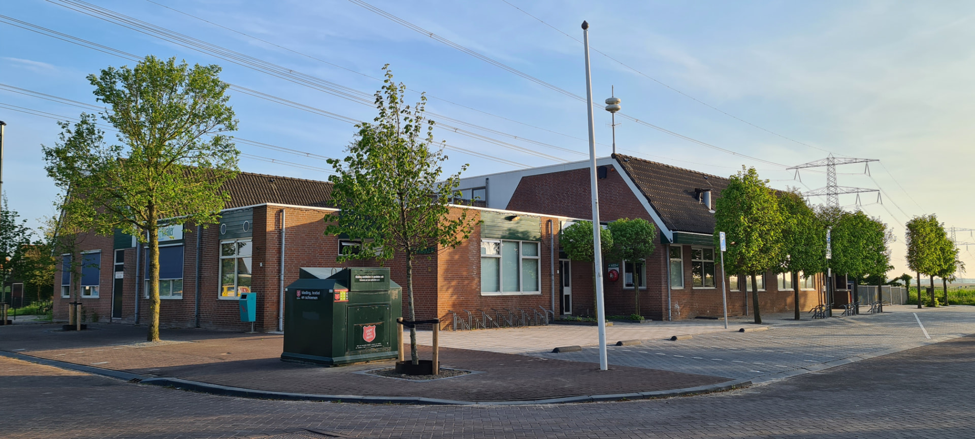 Het dorpsgebouw in Westzaan op de hoek: bakstenen gebouw met bomen, fietsenrekken en vrij zicht op het polderlandschap.